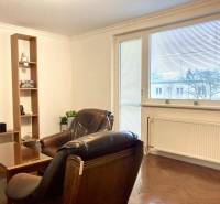 Nappali egy háromszobás lakásban, fa dekoros padlóval, nagy ablakkal és bőr fotelekkel.