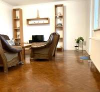 Nappali egy háromszobás lakásban bőr fotelekkel és fa dekorációjú padlóval.