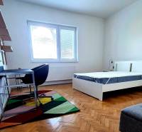 Szoba egy háromszobás lakásban, ággyal, íróasztallal és fa mintázatú padlóval.