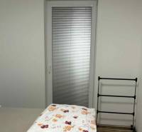 Hálószoba egy kétszobás lakásban erkélyajtóval, ággyal és ruhaszárítóval.