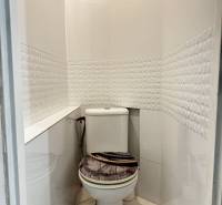 Fürdőszoba WC-vel a háromszobás lakásban, geometrikus mintás csempével és fa dekoros padlóval.