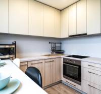 Konyha egy kétszobás lakásban fehér szekrényekkel, mikrohullámú sütővel és főzőlappal.