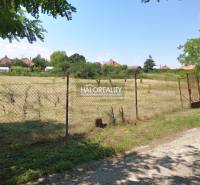 Sík telek kerítéssel körülvéve Marcelová Kertekben, a háttérben házak láthatók.