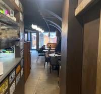 Vendéglátóhely belső tere polcokon tányérokkal, táblákkal, asztalokkal és székekkel.