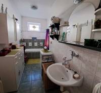 Családi ház fürdőszobája zuhanyzóval, mosdóval és szekrényekkel.