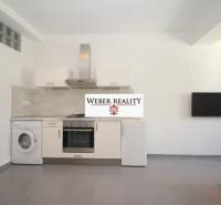 Konyha egy kétszobás lakásban fehér konyhabútorral, mosógéppel és falra szerelt televízióval.