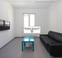 Nappali egy kétszobás lakásban fekete kanapéval, falra szerelt televízióval és alacsony asztallal.