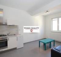 Konyha egy kétszobás lakásban szürke padlóval, konyhabútorral és ülőhellyel.