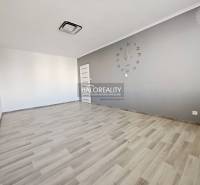 Szoba órával és fa dekorációjú padlóval egy kétszobás lakásban.