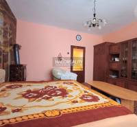 Családi ház belső tere fa bútorokkal, szőnyeggel és színes ágytakaróval ellátott ággyal.