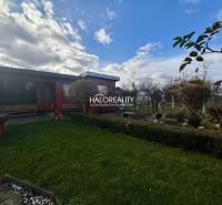 Fából készült pavilon a kertben Iglón, zöld gyep és növényzet mellett.