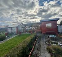 Fából készült házikó a kertekben Iglón, gondozott gyep és bokrok veszik körül.