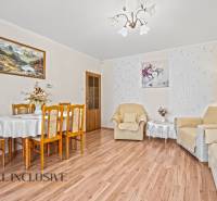 Nappali egy családi házban, fa mintázatú padló, étkezőasztal, fotelek, képek.