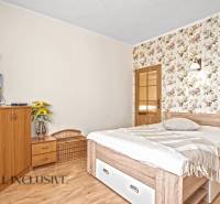 Hálószoba családi házban virágos tapétával, televízióval és fa dekorációjú padlóval.