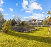 Családi ház kertje Dunaszerdahelyen gyepfelülettel, fákkal és rendezett virágágyással.