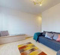 Nappali szürke kanapéval, fa mintázatú padlóval és színes szőnyeggel egy háromszobás lakásban.