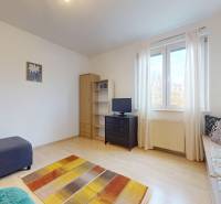 Nappali egy háromszobás lakásban kanapéval, szekrénnyel és fa mintázatú padlóval.