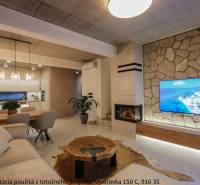 Nappali családi házban kandallóval, kőfalra szerelt TV-vel és fa mintázatú padlóval.