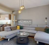 Tágas nappali egy családi házban kanapéval, konyhasarokkal és fa dekorációjú padlóval.