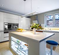 Konyha családi házban központi szigettel, fehér szekrényekkel és készülékekkel.