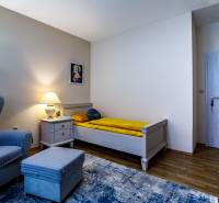 Családi ház szobája fotellel, ággyal, éjjeliszekrénnyel és fa dekorációjú padlóval.