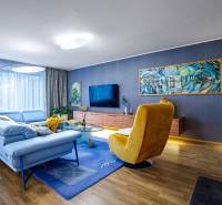 Nappali egy családi házban kék kanapéval, sárga fotellel és fa dekoros padlóval.