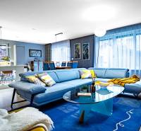 Nappali egy családi házban kék kanapéval, üvegasztallal és fa mintázatú padlóval.