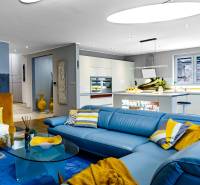 Nappali egy családi házban kék kanapéval és konyhával, fa hatású padlóval.