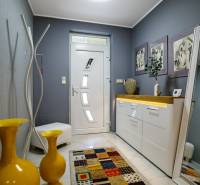 Családi ház előszobája, fehér bútorok, sárga vázák és színes szőnyeg.