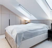 Tetőtéri hálószoba nagy ággyal, éjjeliszekrénnyel és beépített szekrénnyel.
