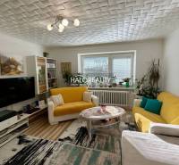 Nappali egy kétszobás lakásban, fa dekoros padlóval, sárga kanapéval és dekorációkkal.