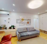 Nappali kanapéval, étkezőasztallal és fa mintázatú padlóval egy háromszobás lakásban.