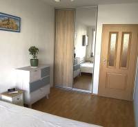 Hálószoba egy kétszobás lakásban fa dekorációjú padlóval, beépített szekrénnyel és komóddal.