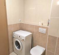 Fürdőszoba egy kétszobás lakásban világos csempékkel, mosógéppel és fali WC-vel.