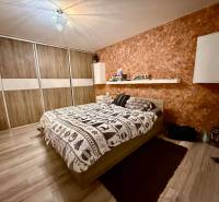 Hálószoba egy kétszobás lakásban ággyal, tárolóhellyel és fa dekorációjú padlóval.