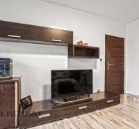 Nappali egy háromszobás lakásban, fa dekoros padlóval és nagy televízióval.