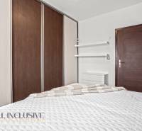 Hálószoba egy háromszobás lakásban ággyal, beépített szekrénnyel és minimalista polcokkal.