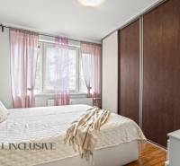 Hálószoba egy háromszobás lakásban ággyal, szekrénnyel és dekoratív párnákkal, fa dekoros padlóval.