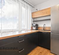 Konyha egy háromszobás lakásban nagy ablakkal, fekete szekrényekkel és fa dekoros padlóval.