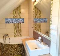 Családi ház fürdőszobája káddal, mosdóval, tükörrel és mozaik díszítéssel.