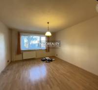 Nappali egy háromszobás lakásban, fa mintázatú padlóval és nagy ablakkal.