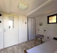 Egyszerű belső tér, fehér házikó, kis asztal, világos padló, ajtó ablakkal, rekreációs tér.