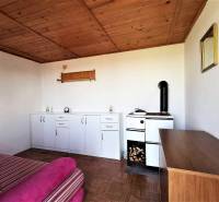 Szoba tűzhellyel, szekrényekkel és kanapéval, otthonossá teszi a faház fa mennyezetét.