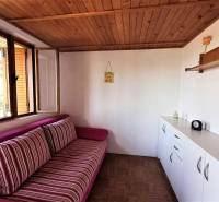 Fahmennyezetes, kényelmes kanapéval és fehér tárolóbútorokkal berendezett házikó.