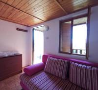 Szoba egy faházban rózsaszín kanapéval, fa mennyezettel és kilátással a nyitott ablakból.