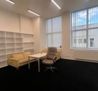 Irodák fekete szőnyeggel, bútorokkal, polcrendszerekkel és nagy ablakokkal.