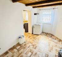 Belső tér fahatású padlóval rendelkező házikóban, mosógép, boltíves bejárat a konyhába.