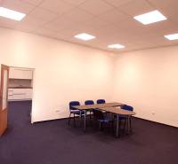 Iroda kék székekkel és asztalokkal, fehér fal, nyitott ajtó egy kis konyhához.