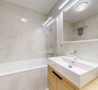 Fürdőszoba egy háromszobás lakásban csempével, káddal, mosdóval és tükörrel.