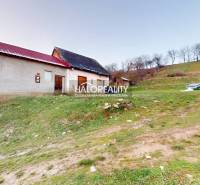 Családi ház Klenócon a domboldalon, mellette egy pad és zöld környezet.